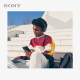 Person using a laptop and smartphone with Sony headphones, sitting outdoors.